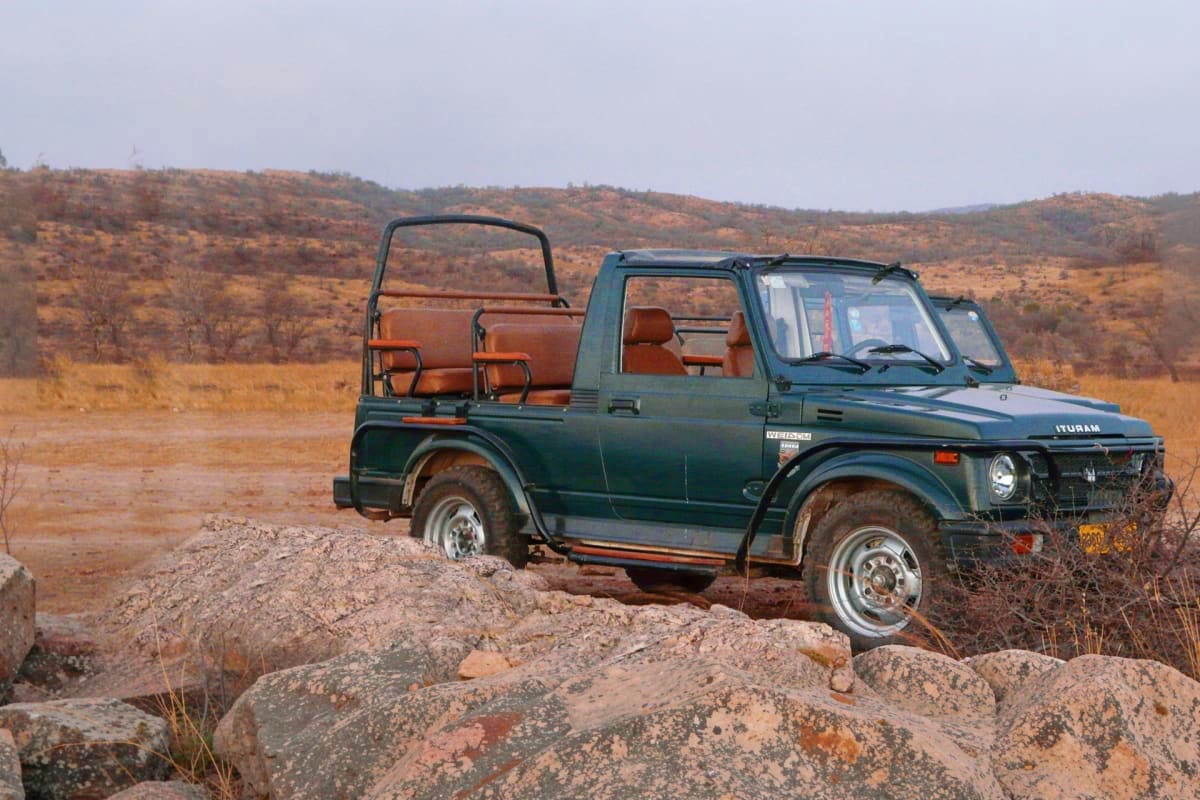 Green Ituram jeep with open-air seating on rocky terrain during Ranthambore safari, arid hillside landscape in background