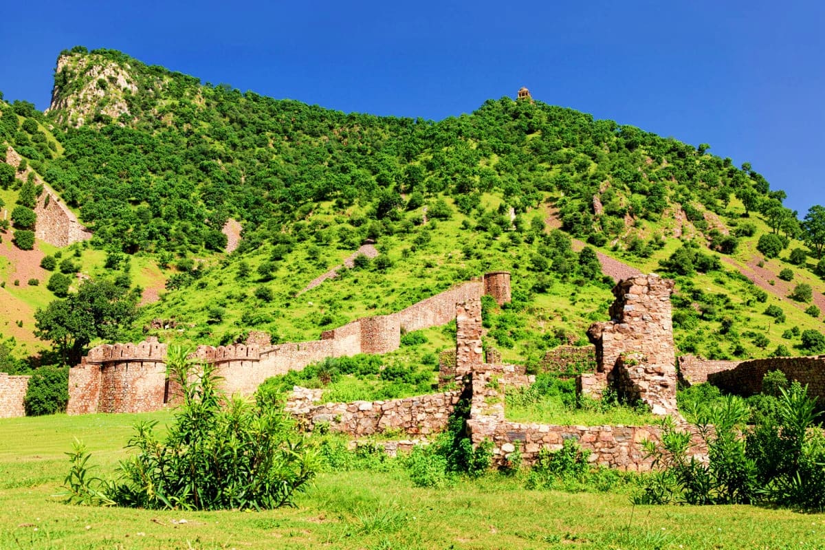 Ranthambore Near By Village Visit Ancient stone ruins with defensive walls and towers nestled among lush green hills under clear blue sky