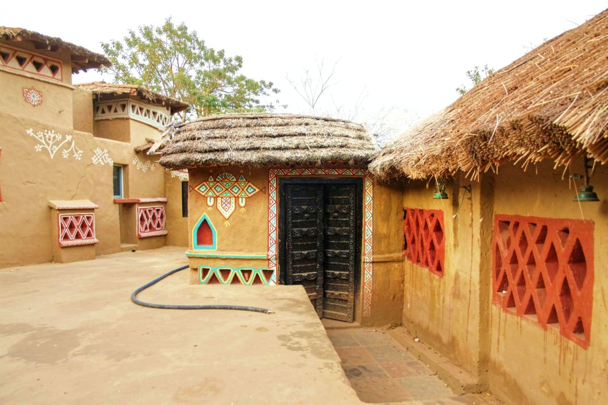 Ranthambore Near By Village Visit Traditional mud-brick village compound with thatched roof huts, colorful geometric patterns, and decorative wooden doors in e