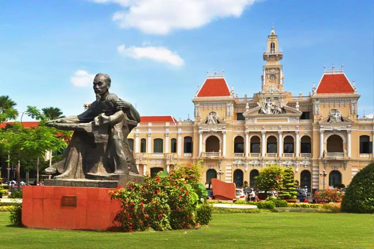 Bronze statue in front of yellow colonial architecture building with red-tiled roofs and clock tower in Ho Chi Minh City
