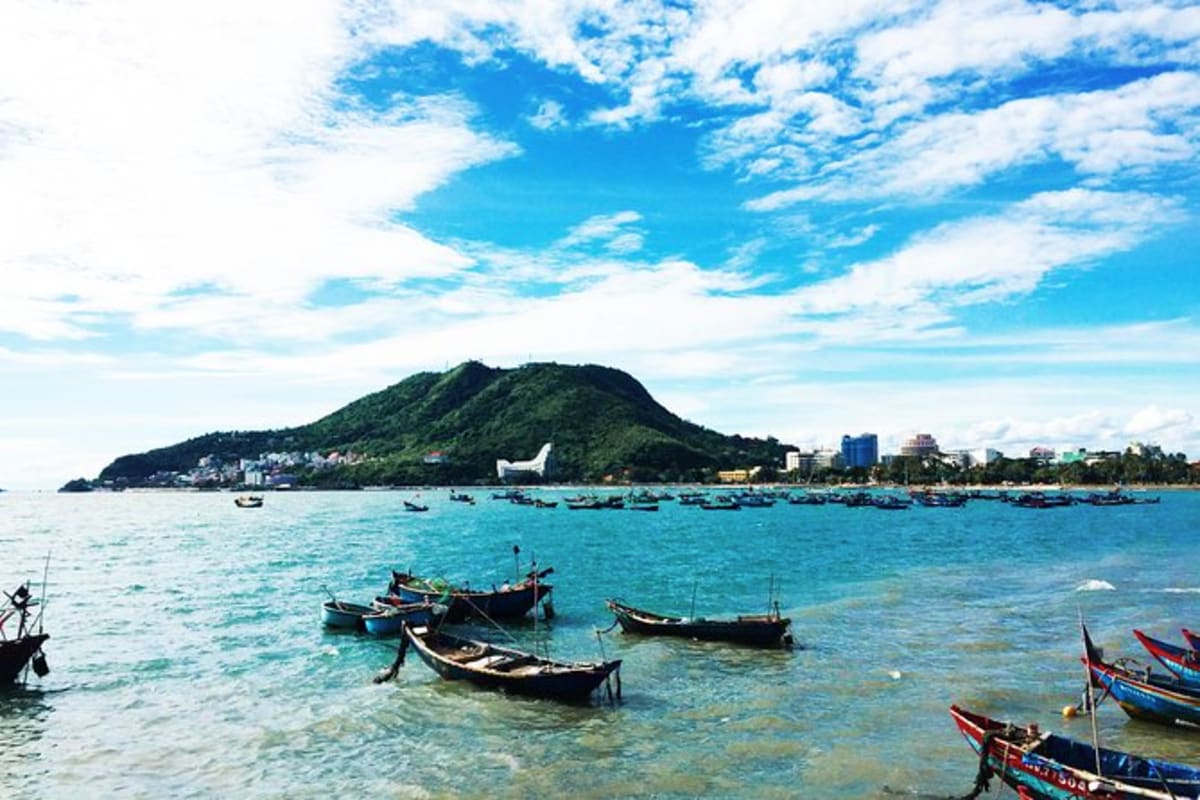 Vung Tau beach Private Tour Full Day Traditional fishing boats anchored in turquoise water at Vung Tau beach with lush green mountain backdrop and coastal city sk