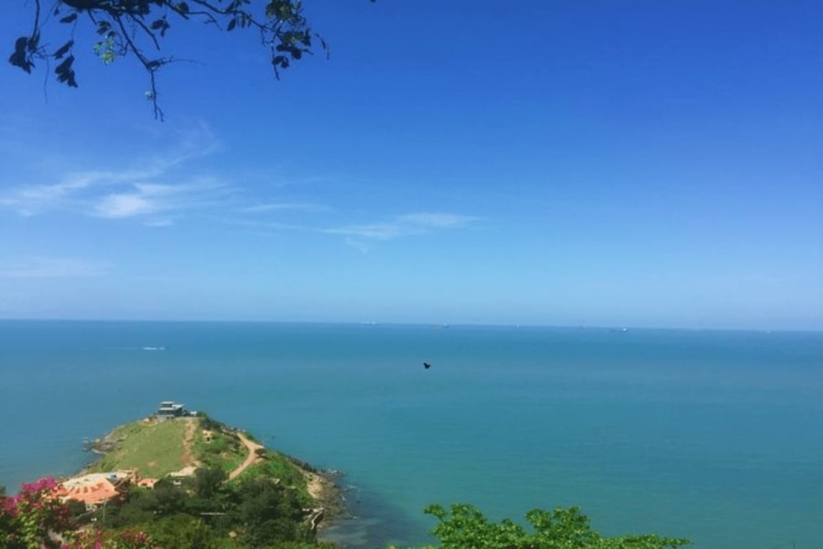 Vung Tau beach Private Tour Full Day Aerial view of a verdant peninsula jutting into turquoise waters of Vung Tau beach under clear blue sky with flowering plants