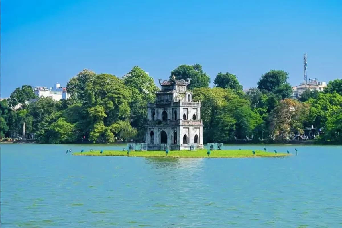 Hanoi Full Day Tour Turtle Tower on Hoan Kiem Lake in Hanoi with green water, trees, and visitors on the shore