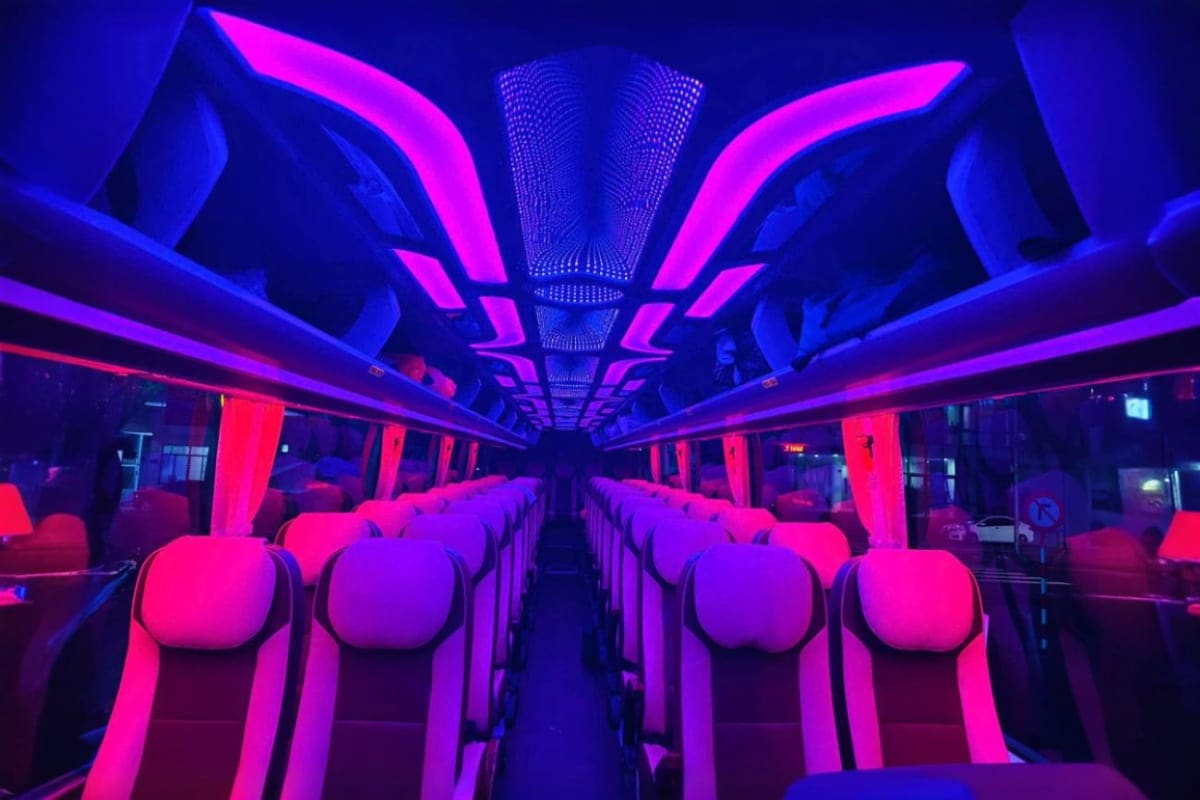 Modern coach bus interior with neon pink and blue LED lighting, empty seats, and illuminated ceiling panels for private trans