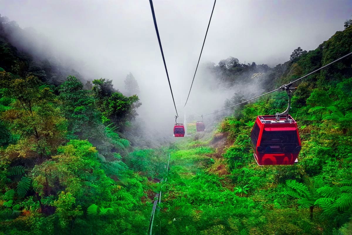 Genting Highlands Tour with Awana Cable Car and Batu Caves Visit Red cable car descending misty mountain forest in Genting Highlands with lush green vegetation and fog-covered valleys below