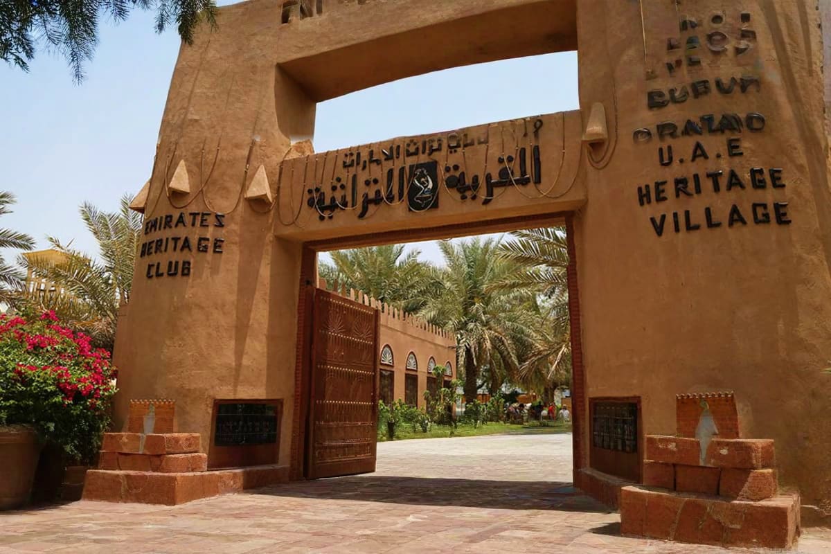 Emirates Heritage Club entrance gate with Arabic calligraphy, wooden doors, and palm trees in Abu Dhabi