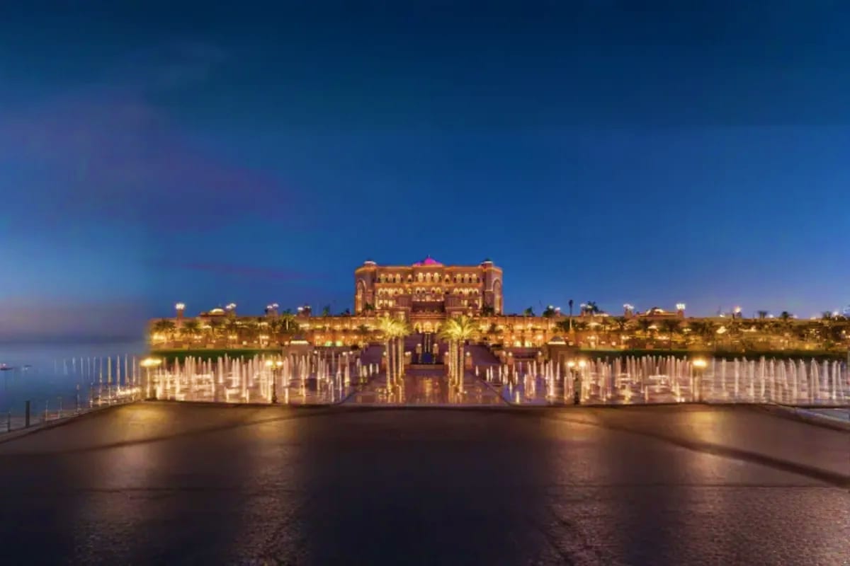 Emirates Palace hotel illuminated at dusk with fountain displays and palm trees along the waterfront in Abu Dhabi