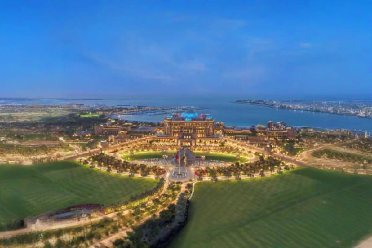 Aerial view of Emirates Palace luxury hotel with manicured gardens, fountains, and harbor in Abu Dhabi cityscape