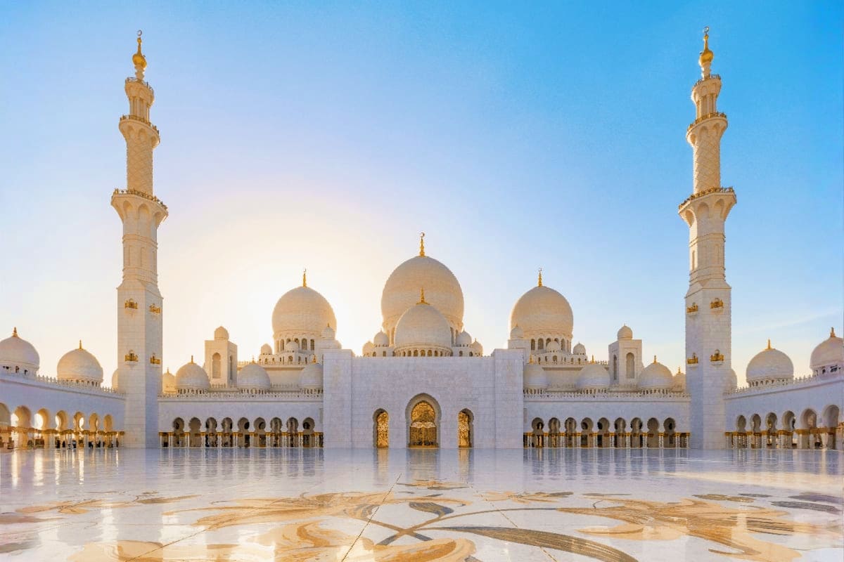 Sheikh Zayed Grand Mosque in Abu Dhabi with white marble courtyard, golden domes, and tall minarets under blue sky