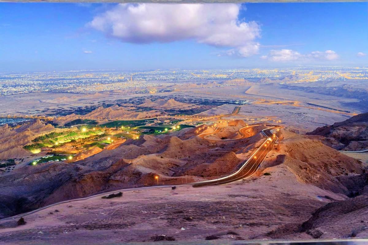 Aerial view of Al Ain desert landscape with illuminated highway, oasis vegetation, and sprawling city in the distance under b