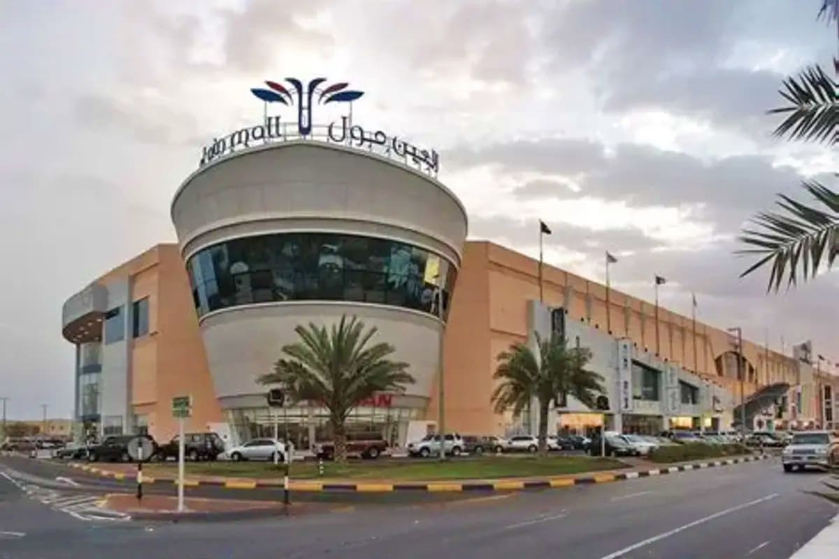 Lulu Mall Al Ain exterior with distinctive cylindrical white tower, palm trees, and parked vehicles under cloudy sky