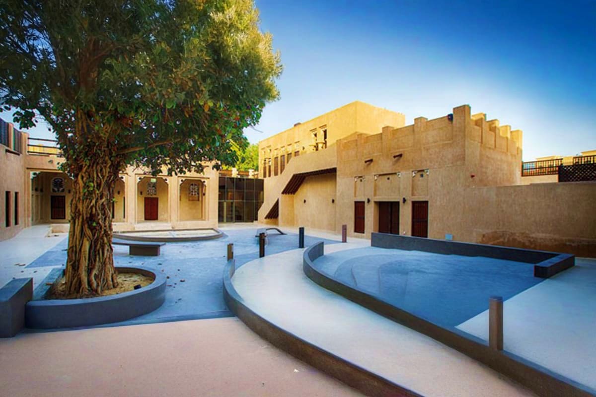 Al Shindagha Museum Courtyard of Al Shindagha Museum with traditional Arabic architecture, mature tree, and blue water features under clear blue