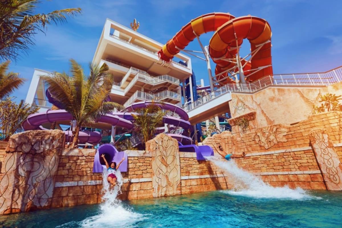 People sliding down purple and orange water slides into a pool at Atlantis Aquaventure Waterpark with modern hotel building a
