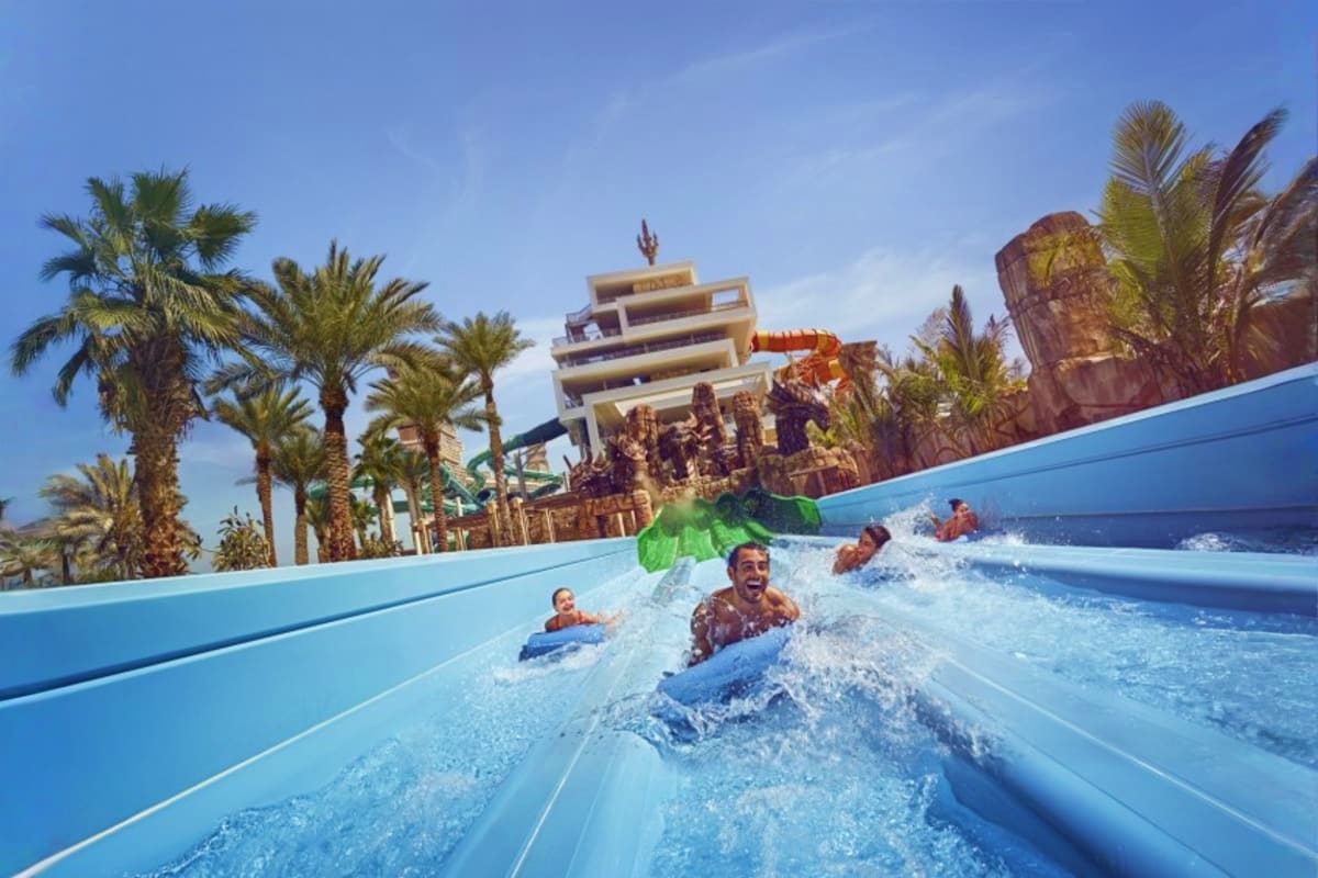 Families riding a wave water slide at Atlantis Aquaventure Waterpark with palm trees and themed architecture in background