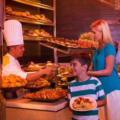 Baker serving freshly baked pastries to a boy and woman at an Atlantis bakery counter display