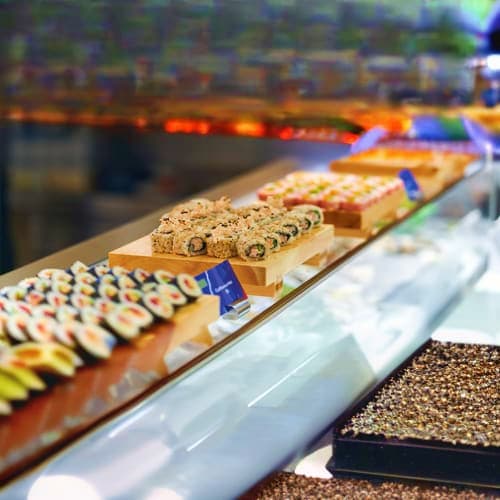 Sushi and rolls displayed on a conveyor belt at a restaurant, with various prepared dishes visible along the moving line