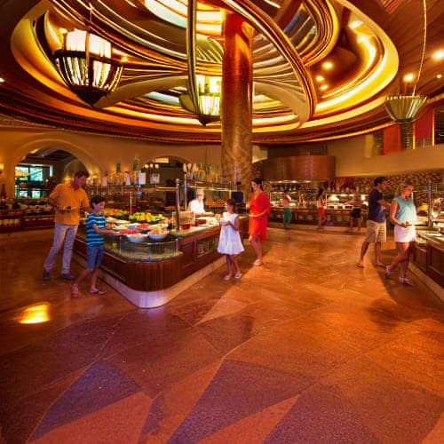Elegant indoor dining buffet at Atlantis resort with golden circular ceiling, central pillar, and guests selecting food from