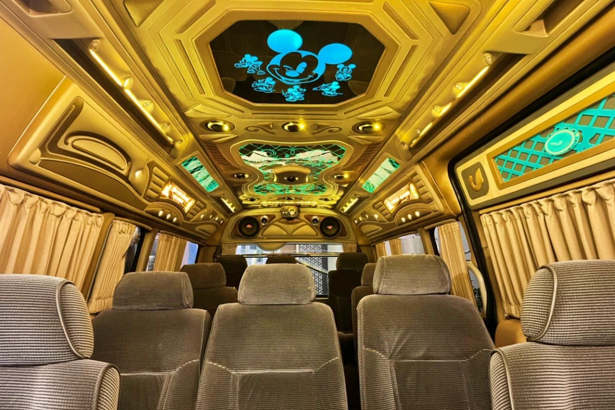 Bangkok Airport to Hua Hin Hotel Luxury charter bus interior with gold ceiling, Mickey Mouse character display, cream-colored seats and curtains facing forwar