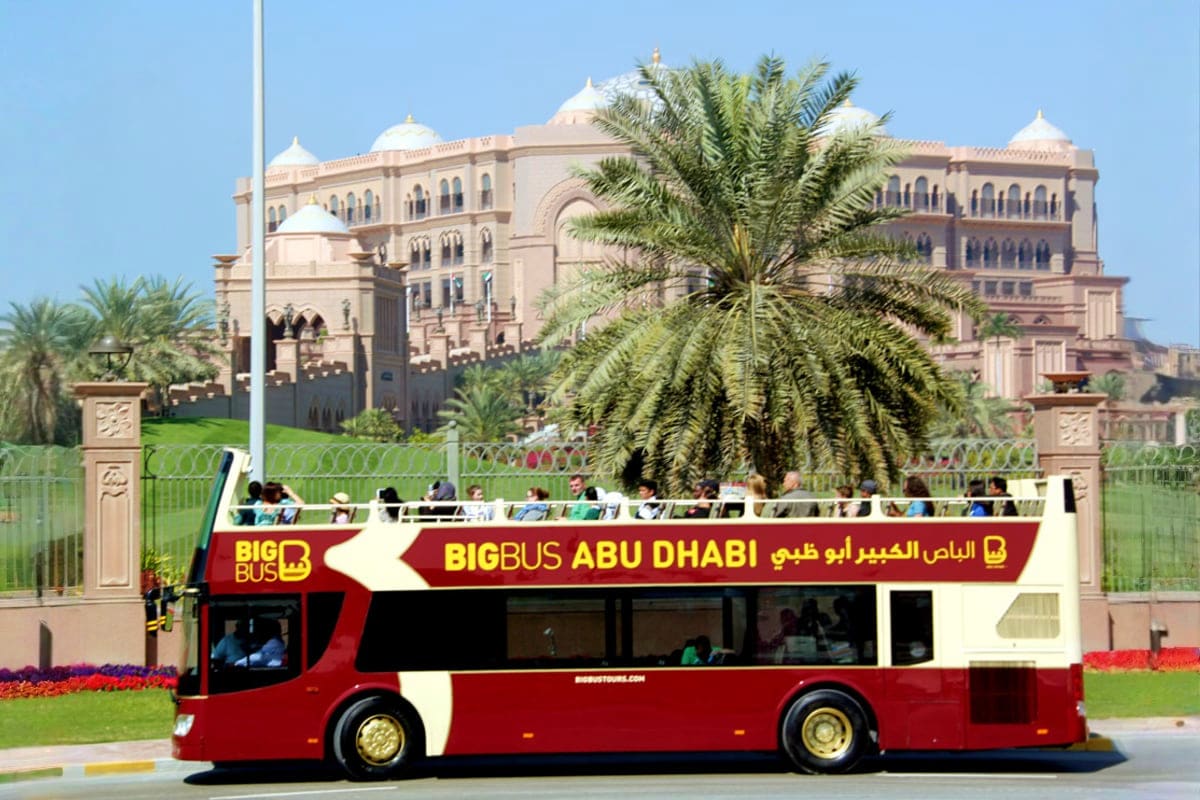 Big Bus Sightseeing Tour Red and white Big Bus Abu Dhabi sightseeing tour vehicle in front of Emirates Palace hotel with palm trees and clear blue sky