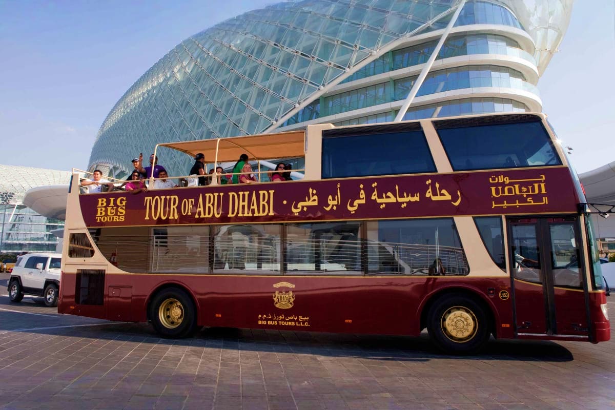 Big Bus Sightseeing Tour Double-decker red and cream tour bus with passengers on top deck outside modern curved glass building in Abu Dhabi