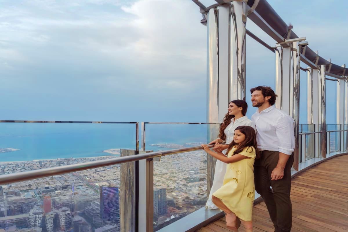 Family of three standing on observation deck overlooking Dubai cityscape and coastline from Burj Khalifa