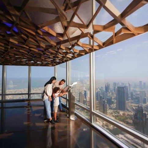 Couple viewing cityscape from observation deck of Burj Khalifa with floor-to-ceiling windows overlooking Dubai skyline