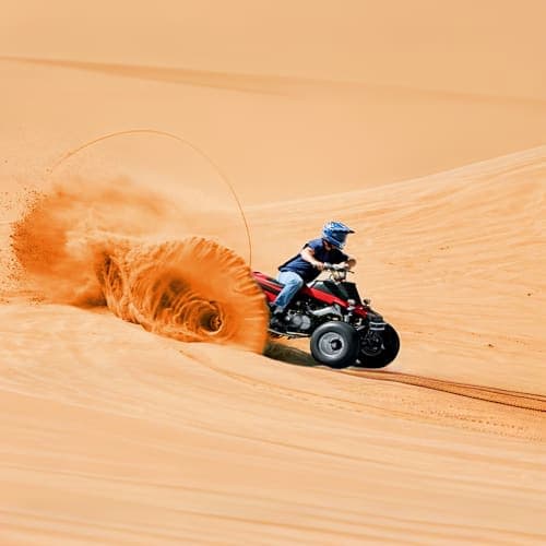 Quad biker riding through sand dunes creating large dust cloud in desert landscape