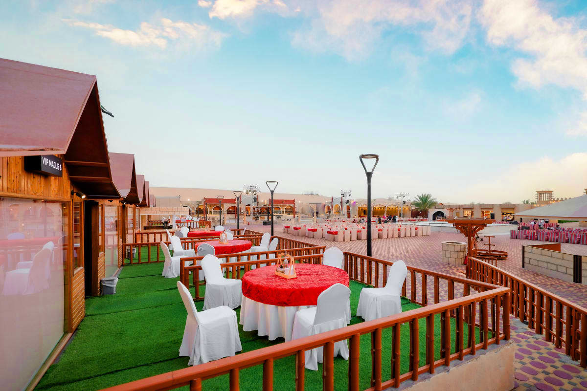 Desert Safari with Quad Biking Outdoor event venue with red-clothed round tables, white chairs, and green artificial grass setup in desert landscape with mo