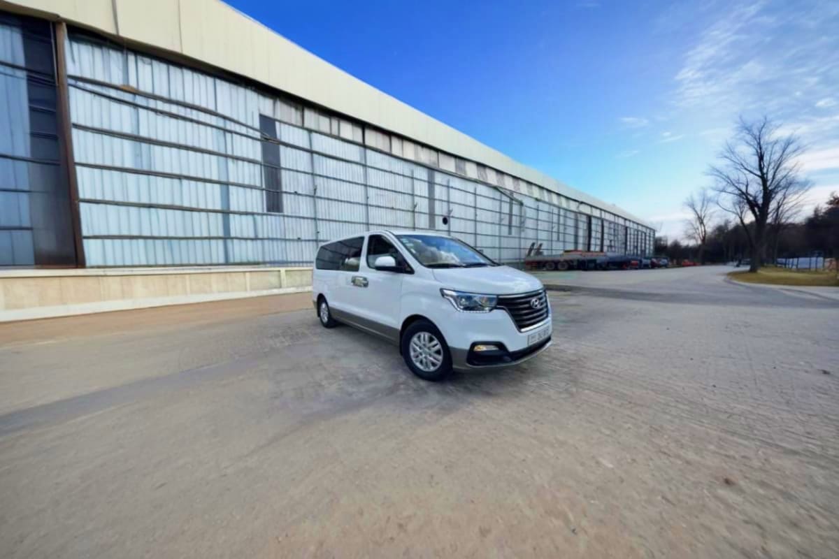 Donmueang International Airport Pickup White Hyundai passenger van parked on concrete lot in front of industrial warehouse building under clear blue sky