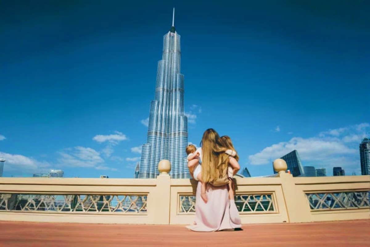 Woman holding child on observation deck with Burj Khalifa tower in background, Dubai skyline view