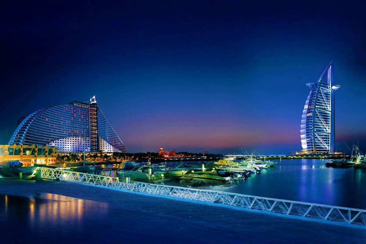 Illuminated Burj Al Arab and Jumeirah Beach Hotel at dusk reflecting in calm water with marina and bridges in Dubai