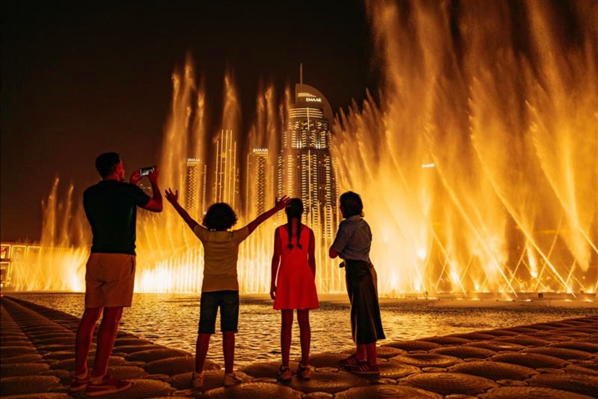 Dubai Fountain Show and Lake Ride Family watching illuminated Dubai Fountain water show at night with modern skyscrapers in background