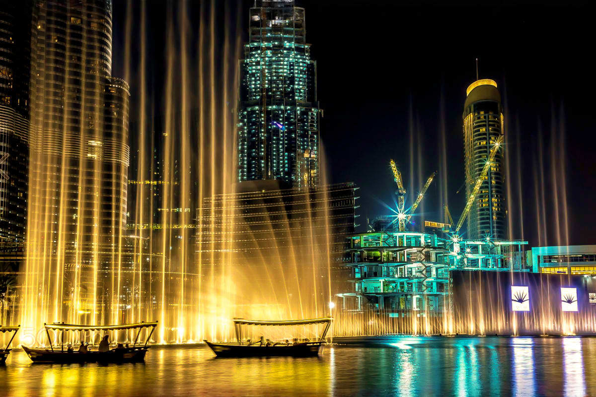 Dubai Fountain Show and Lake Ride Illuminated fountain jets shooting water high into the night sky with traditional wooden boats in the foreground and lit skys