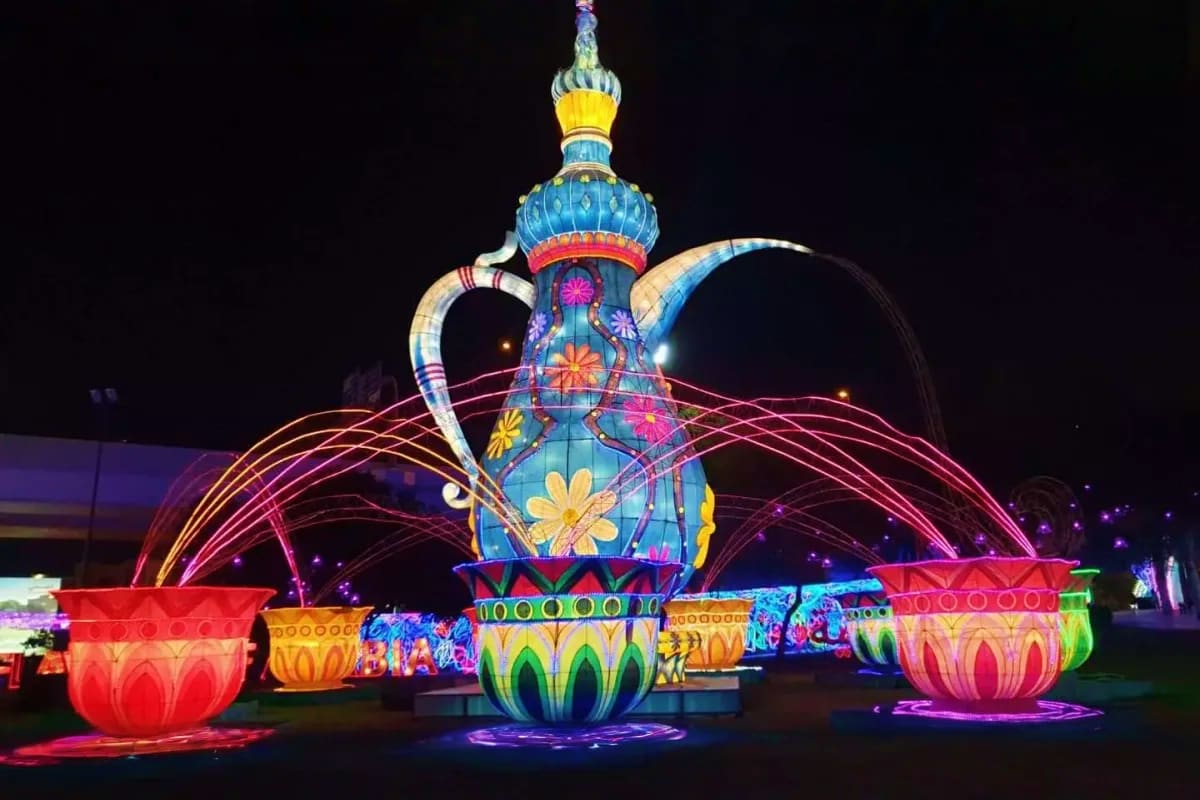 Glow Garden Illuminated genie lamp light sculpture with colorful flowers and arching light streams at night, surrounded by glowing lotus-