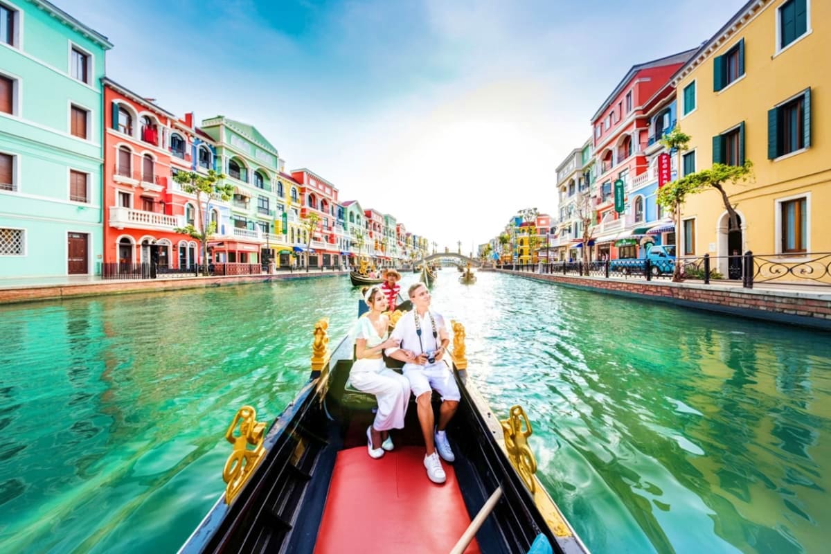 Grand World with Gondola Ride Couple riding in a gondola on a canal surrounded by colorful Renaissance-style buildings in Venice, Italy