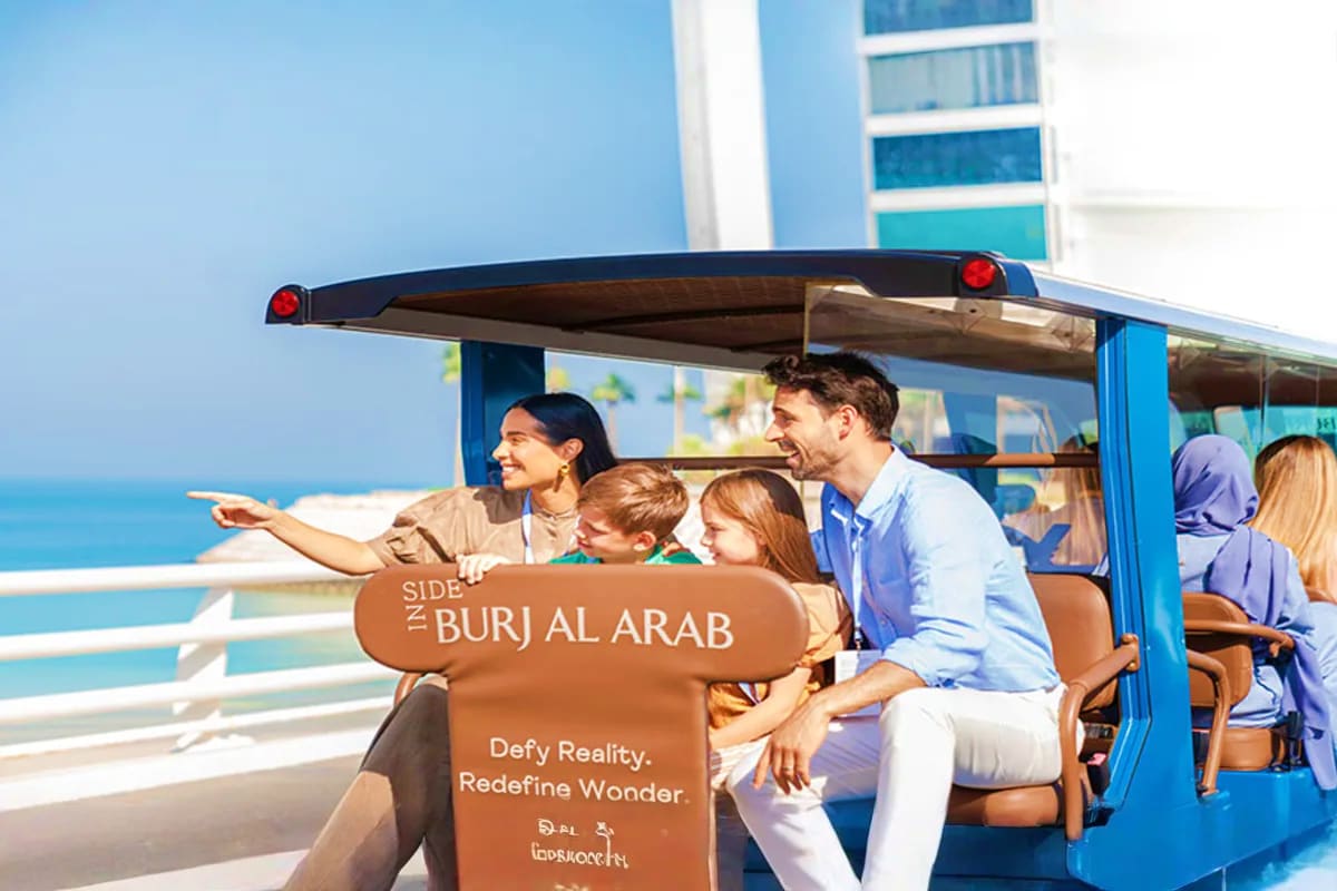 Guided Inside Burj Al Arab Tour Family enjoying an open-air tram tour with ocean views and Burj Al Arab branding visible on the vehicle
