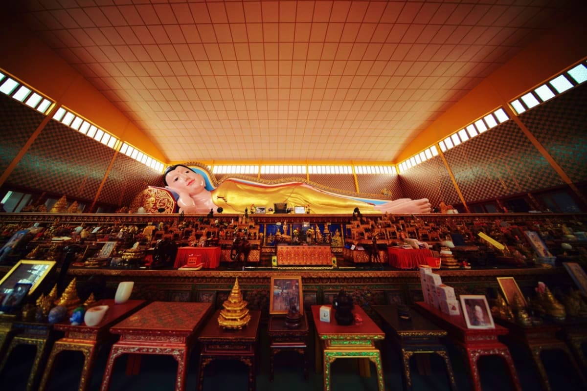 Half Day Penang City Tour Interior of Wat Chaiya Mangalaram temple in Penang with large golden reclining Buddha statue and ornate red wooden decoration