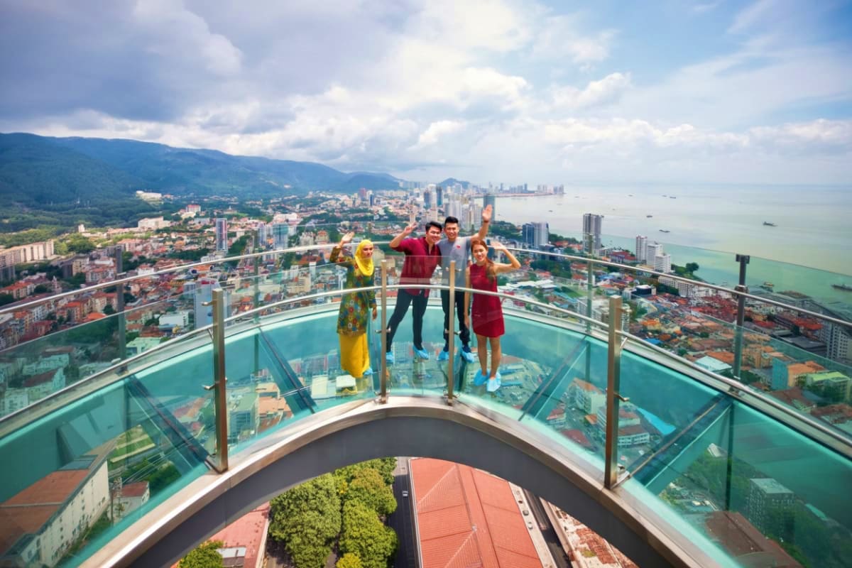 Half Day Penang City Tour Family of four posing on glass skywalk observation deck overlooking Penang city skyline, coastal waters, and mountains