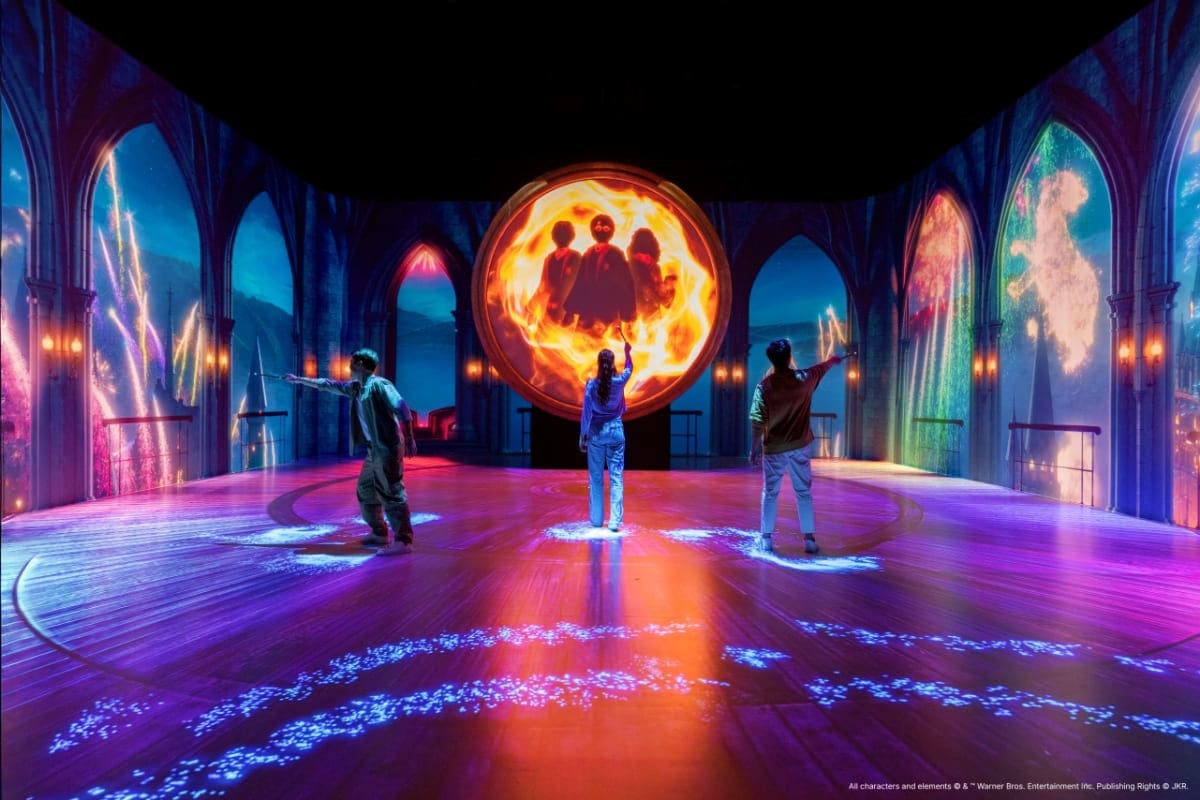 Visitors standing in a gothic cathedral interior with glowing neon light installations and magical projections on the floor a