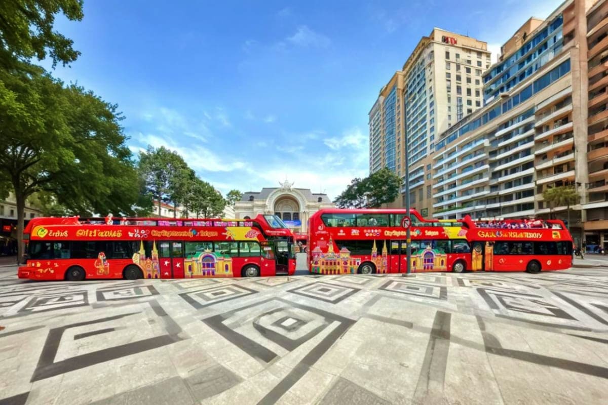 Red double-decker hop-on hop-off tour buses parked in Ho Chi Minh City square with colonial architecture and trees in backgro