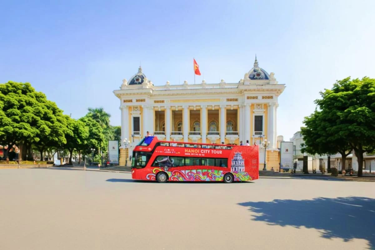 Red double-decker Hanoi City Tour bus in front of the yellow and white colonial Opera House with Vietnamese flag