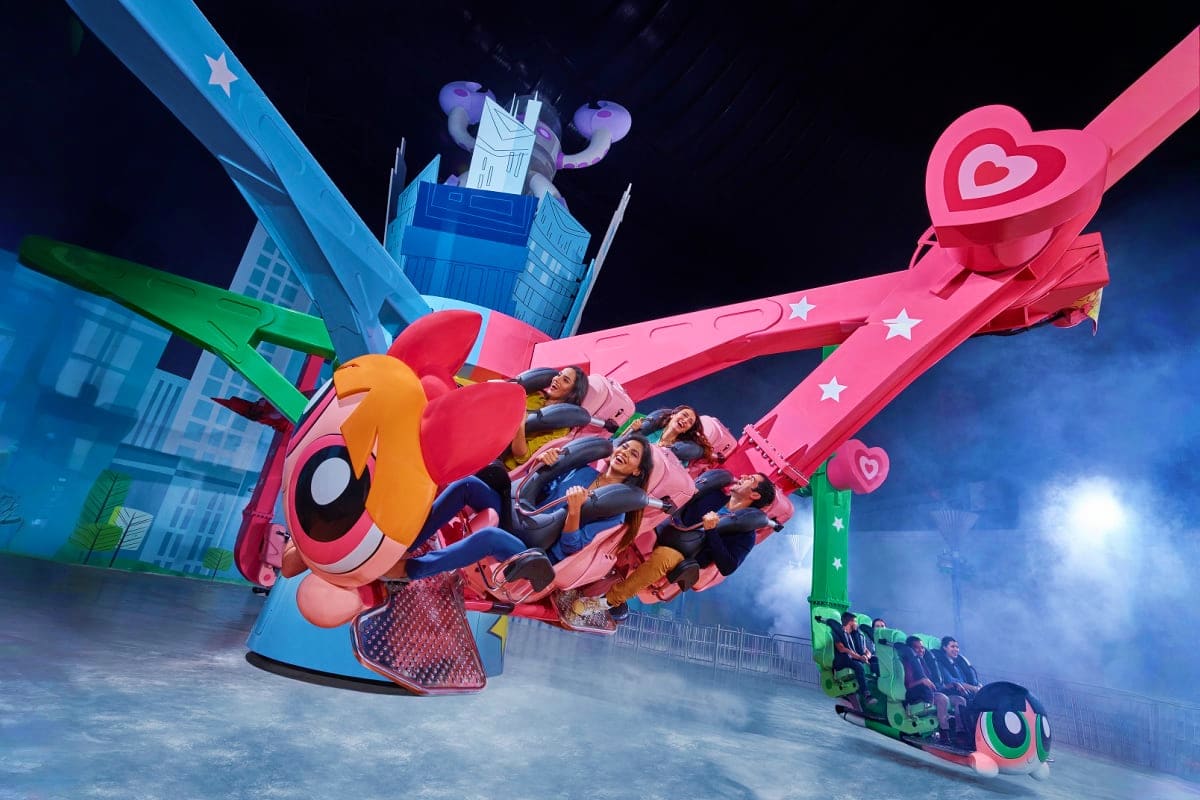 IMG Worlds of Adventure Families riding pink heart-shaped ride at IMG Worlds of Adventure theme park with colorful cartoon buildings in background