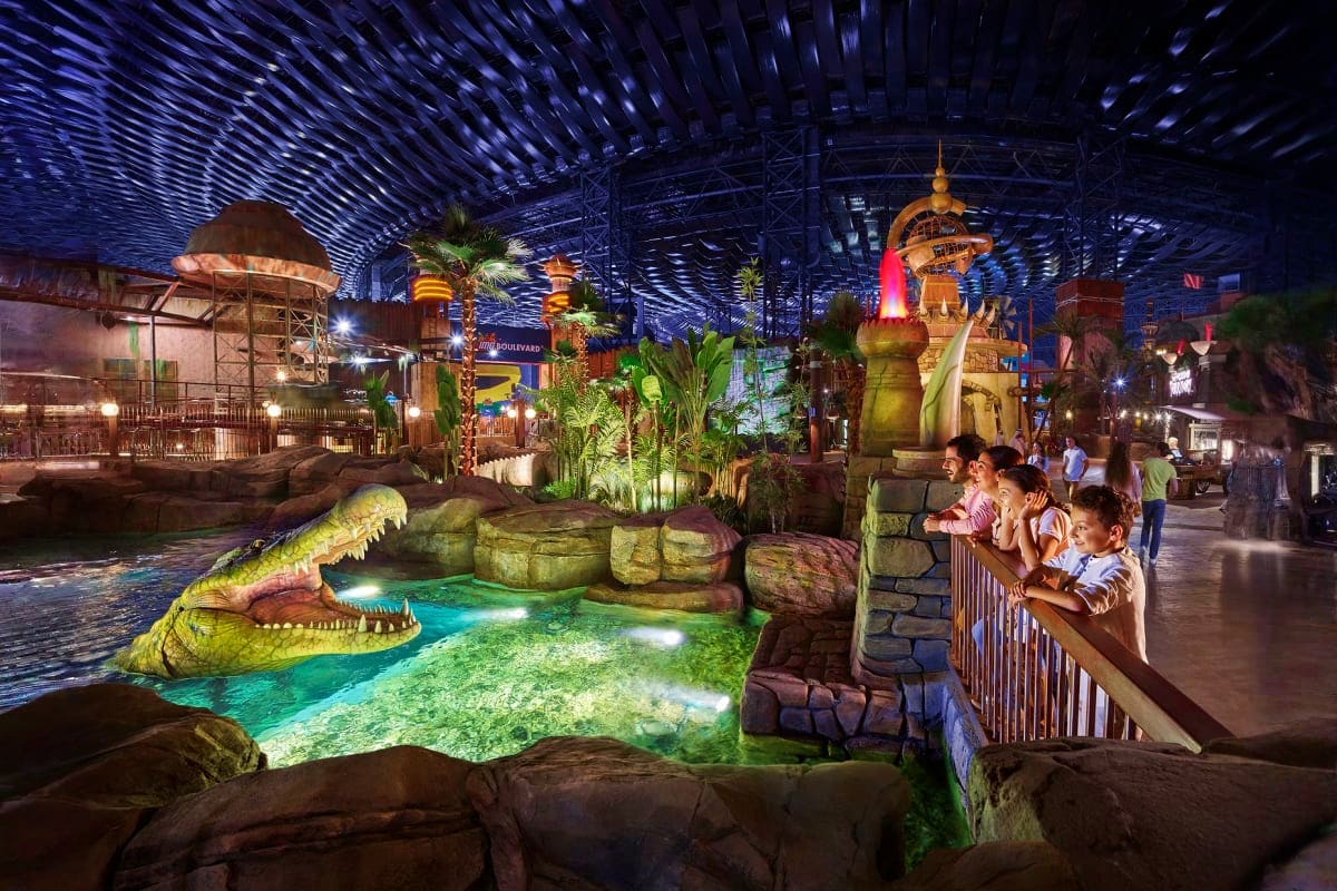 IMG Worlds of Adventure Visitors viewing a large animatronic crocodile in glowing turquoise water at IMG Worlds of Adventure indoor theme park