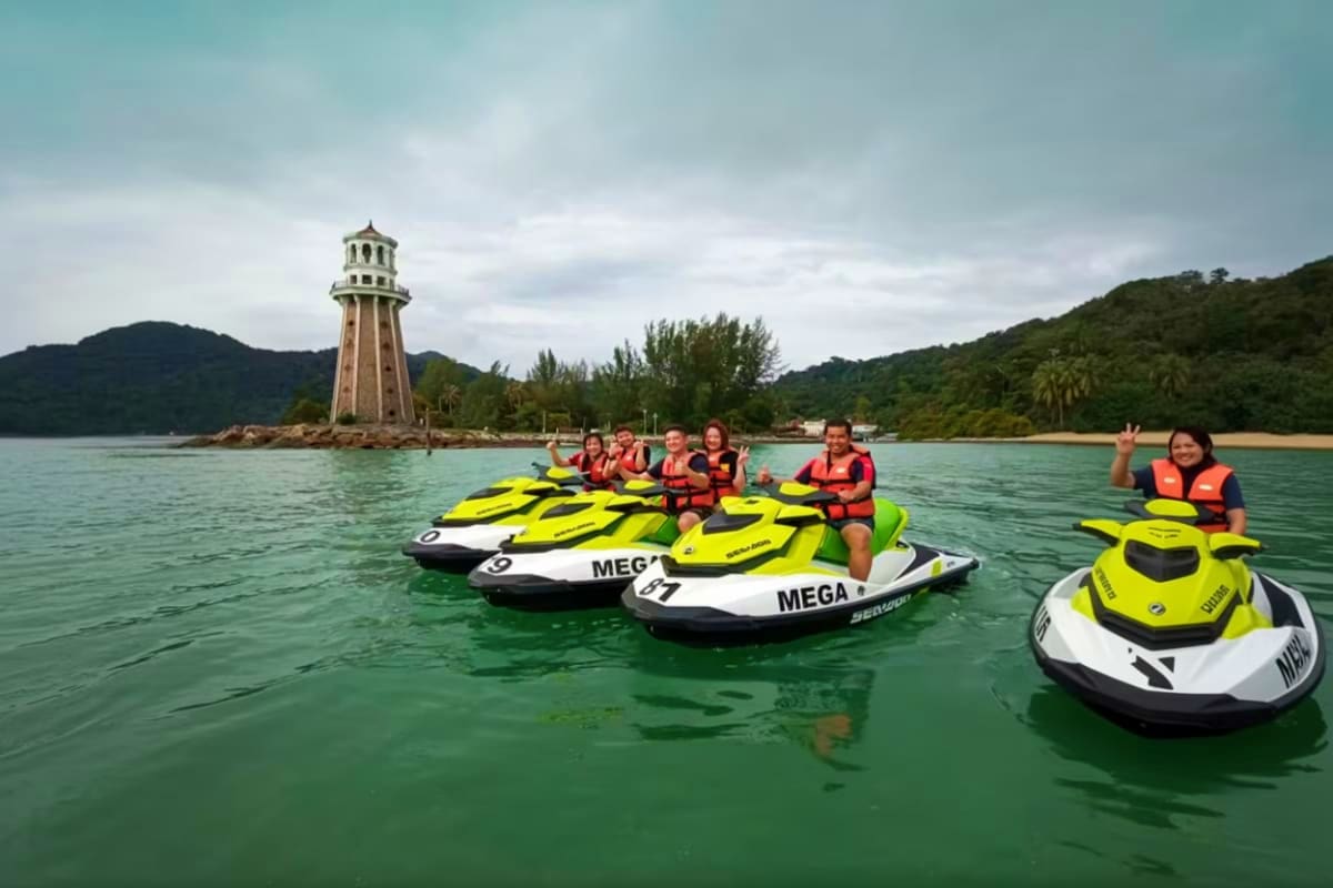 Jet ski at Cenang Beach Group of tourists on bright yellow and white jet skis at Cenang Beach with red-striped lighthouse in background and forested