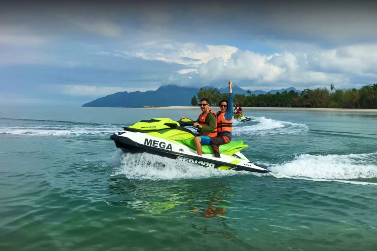 Jet ski at Cenang Beach Two people riding a neon green jet ski in shallow waters at Cenang Beach with mountains and palm trees in the background
