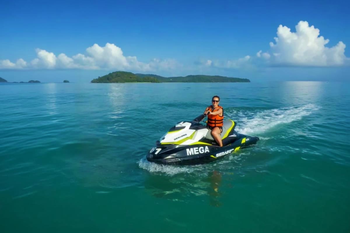 Jet ski at Cenang Beach Person riding a jet ski in turquoise water at Cenang Beach with tropical islands visible in the distance under blue sky
