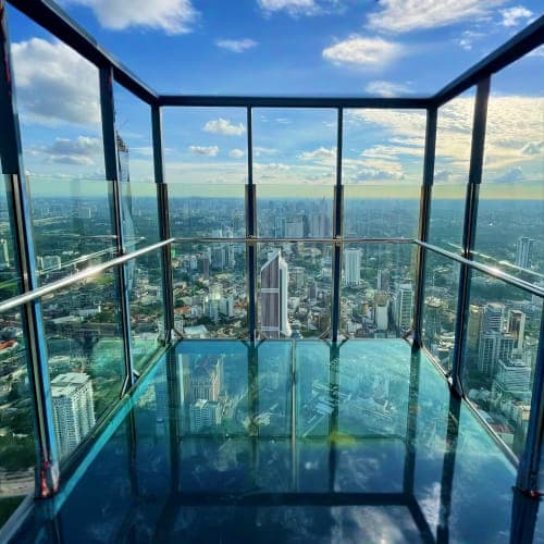 Glass observation deck with transparent floor overlooking sprawling Kuala Lumpur cityscape and skyline under blue sky