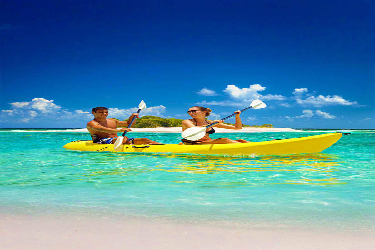 Kayaking Experience in Dubai Two people paddling a yellow kayak in turquoise tropical waters with white sand beach and green island in background