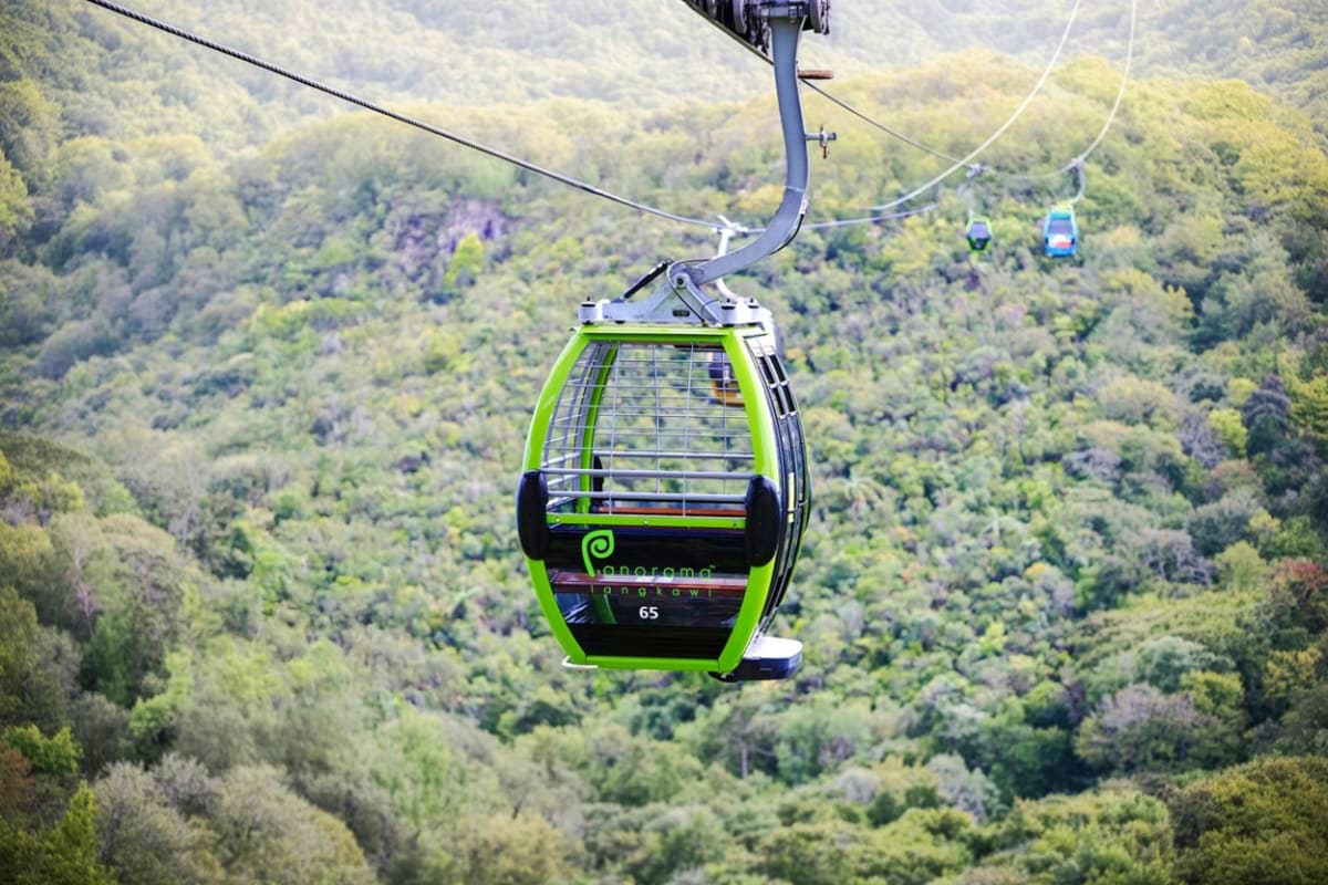Bright green cable car suspended above lush green forested mountains in Langkawi with additional gondolas visible in the dist