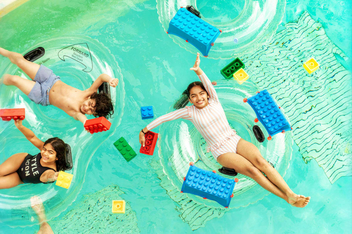 Children floating on colorful LEGO brick-shaped pool floats in turquoise water at Legoland Water Park, overhead view